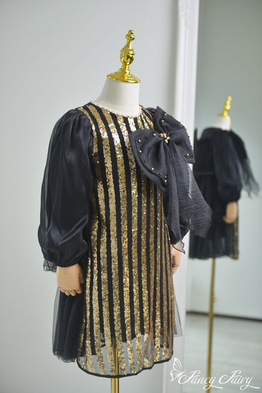 Side view of black and gold sequin dress with puff sleeves and bold black bow.