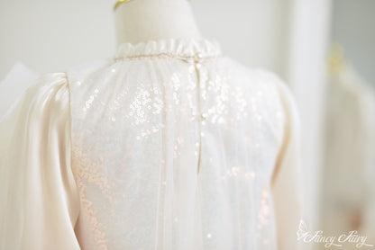 Back close-up of apricot girls' dress featuring sequin mesh overlay, pearl button closure, and ruffle neckline trim.