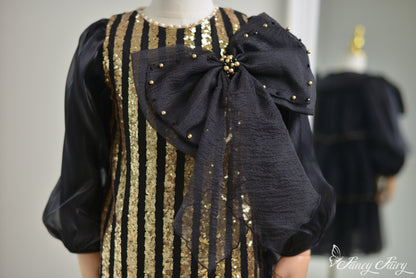 Close-up of sequin stripes and black bow detail with gold pearls and textured fabric.