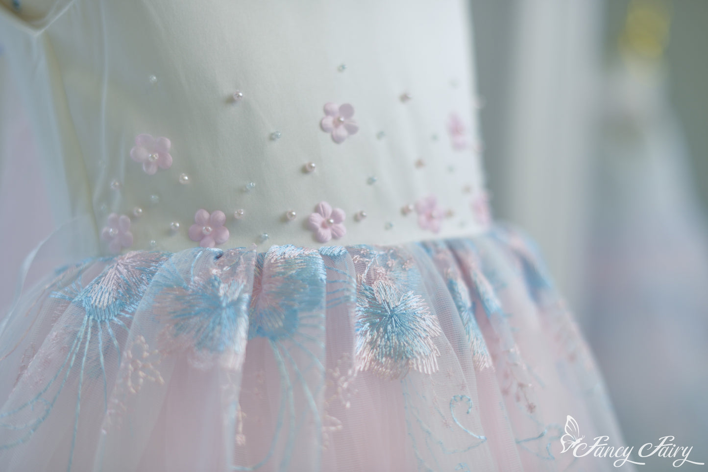 Detail of bodice embroidery and gathered waist seam with pink floral accents.