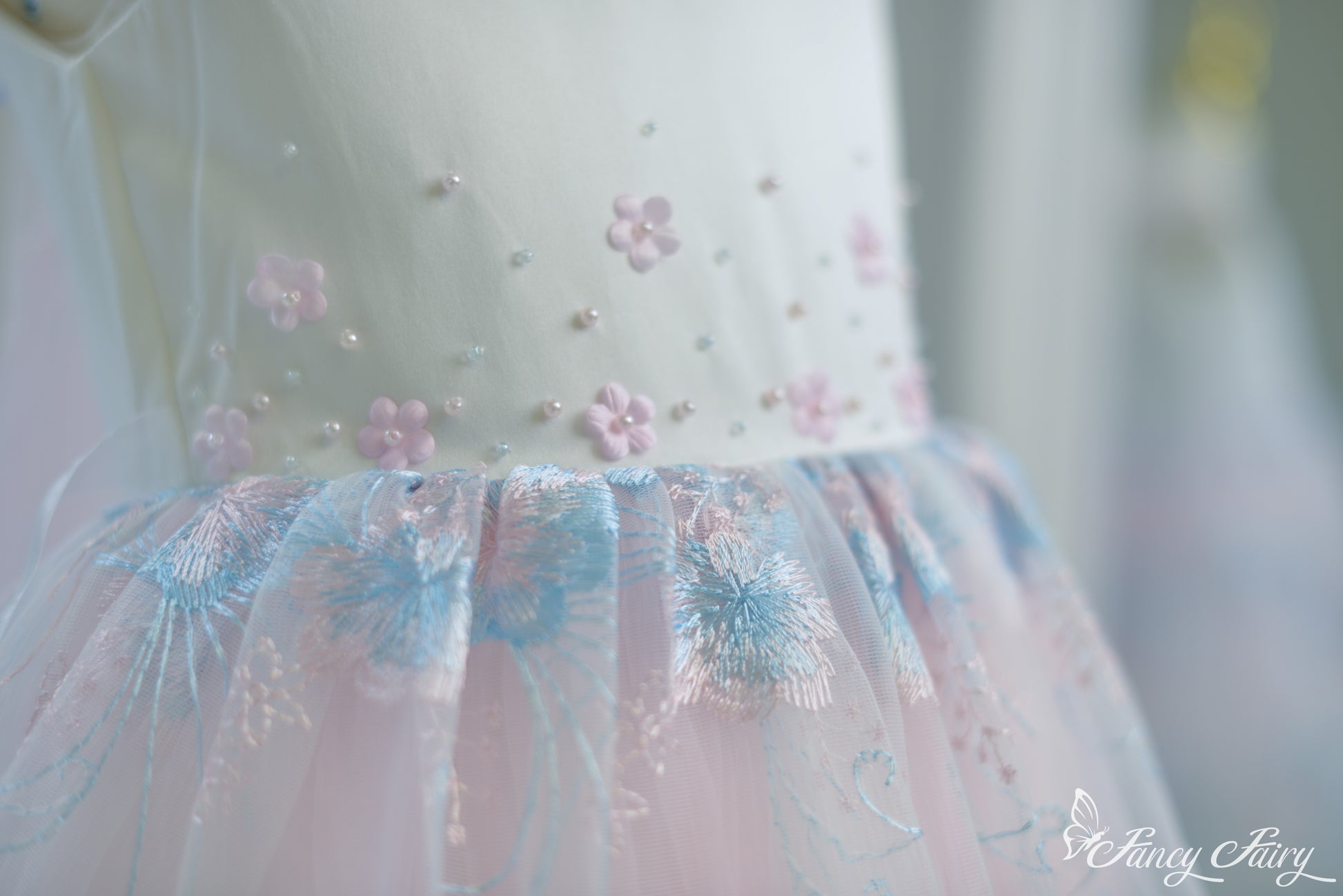Detail of bodice embroidery and gathered waist seam with pink floral accents.