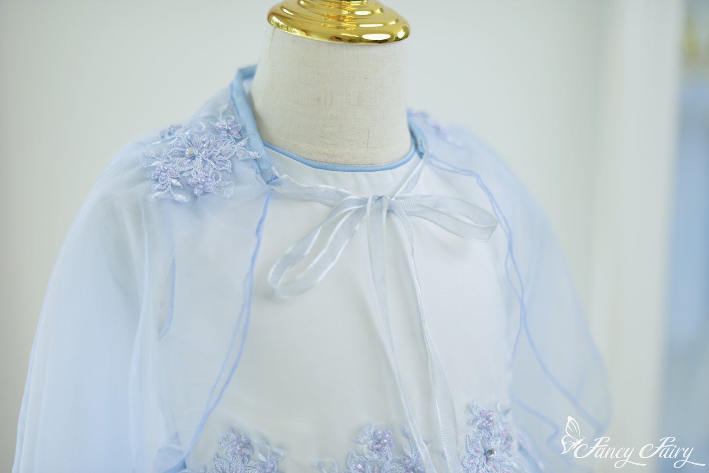 Close-up of shoulder embroidery and ribbon neckline on blue cape dress.