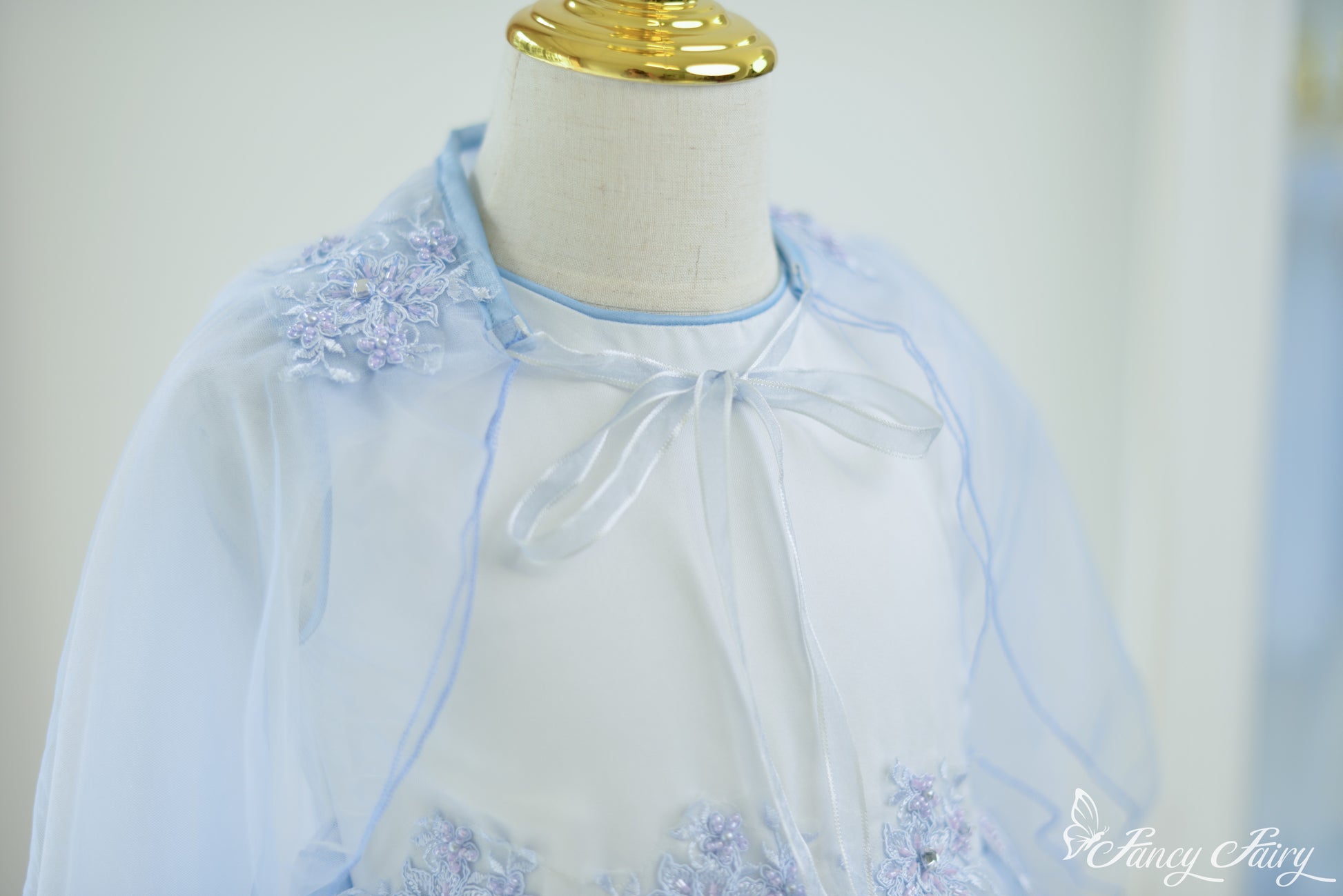 Close-up of shoulder embroidery and ribbon neckline on blue cape dress.