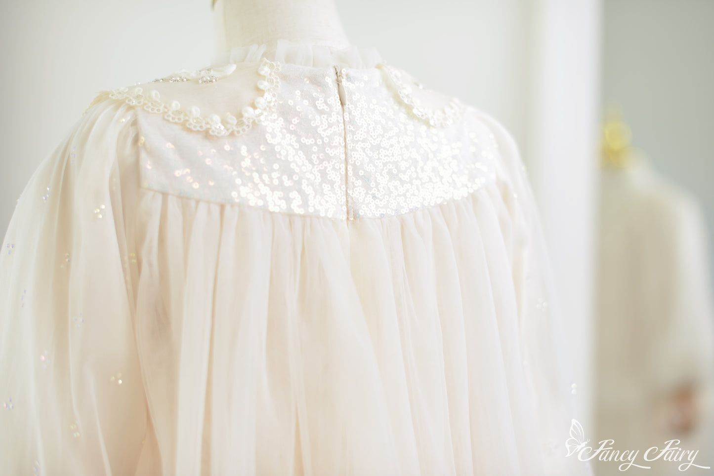 Back close-up of ivory lace dress with sequin yoke, soft tulle gathering, and delicate floral trim.