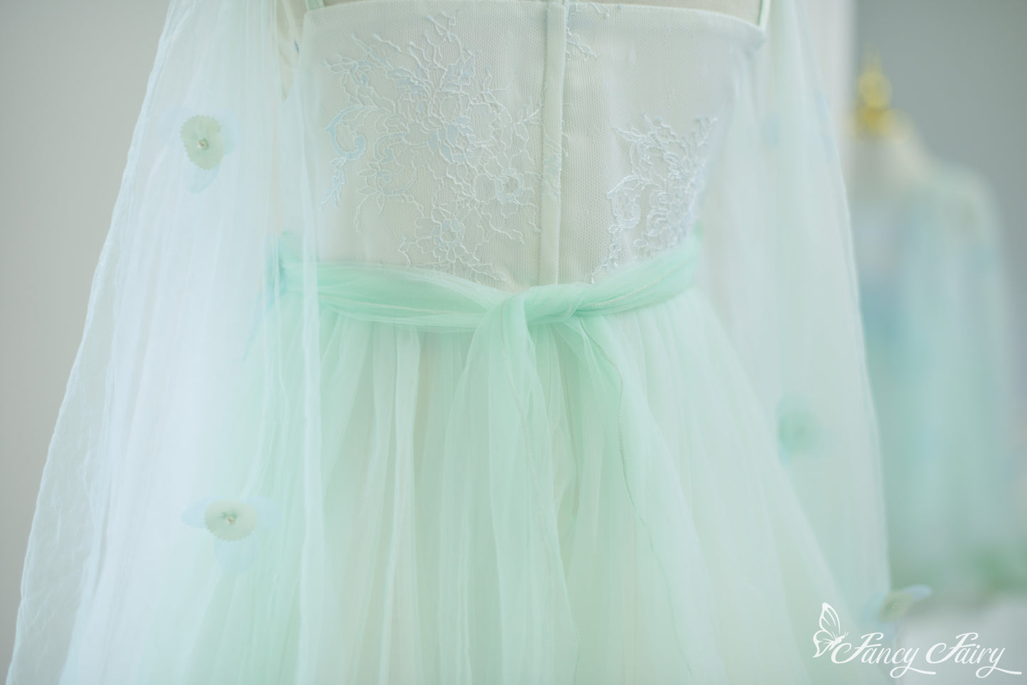 Detail of mint green waist bow and translucent cape with sewn flower appliqués.