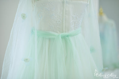 Detail of mint green waist bow and translucent cape with sewn flower appliqués.