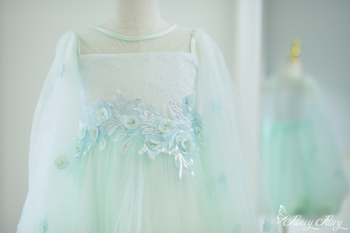 Front close-up of mint green girls' dress with floral embroidery, sheer sleeves and floral embroidery.