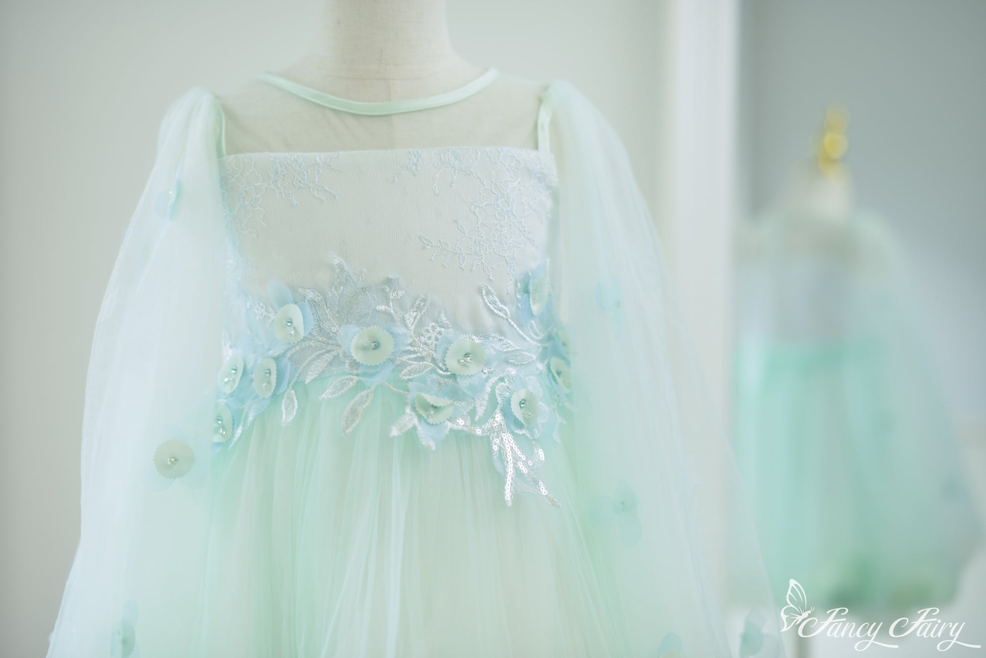Front close-up of mint green girls' dress with floral embroidery, sheer sleeves and floral embroidery.