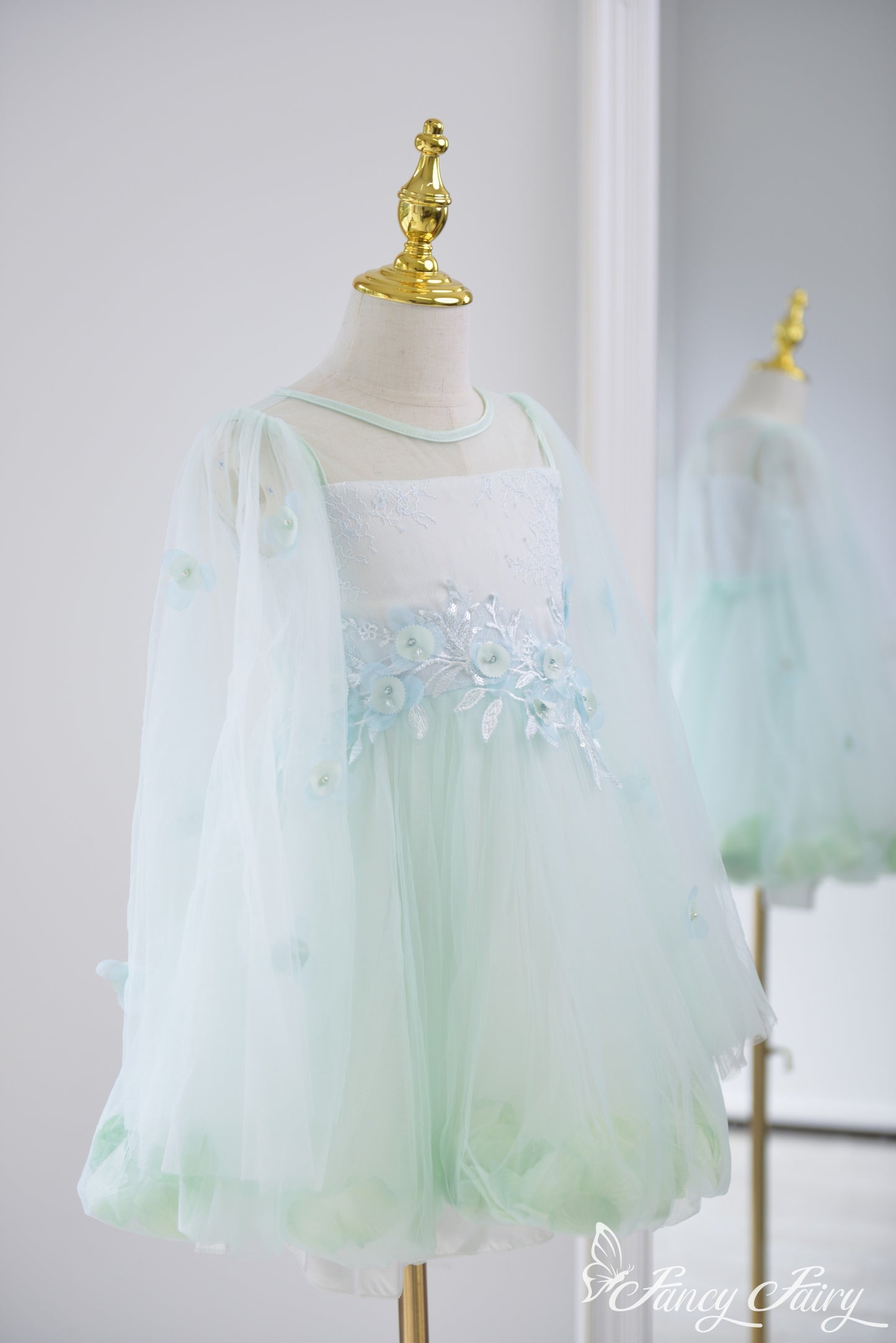 Side view of mint green girls' dress with sheer sleeves, floral embroidery, and petal hem.