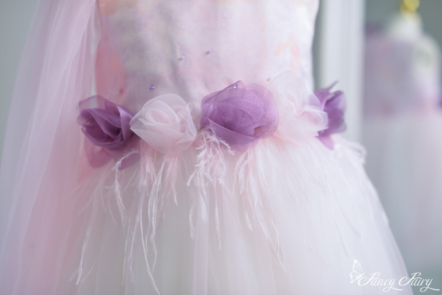 Close-up of waist detail featuring feather trim and layered pink-purple 3D flowers.