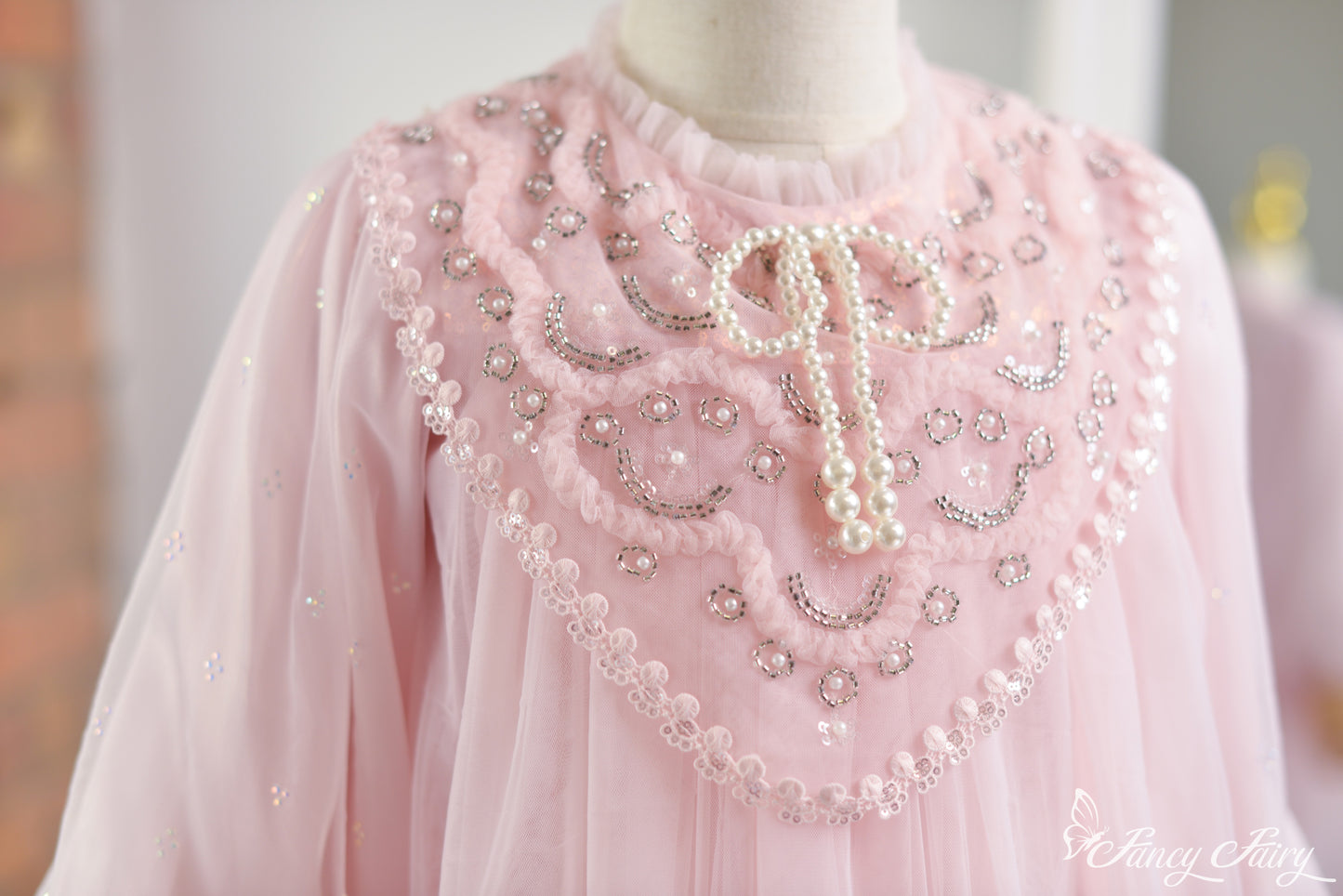Close-up of pink lace dress front chest panel with pearl beading and bow-tie neckline.