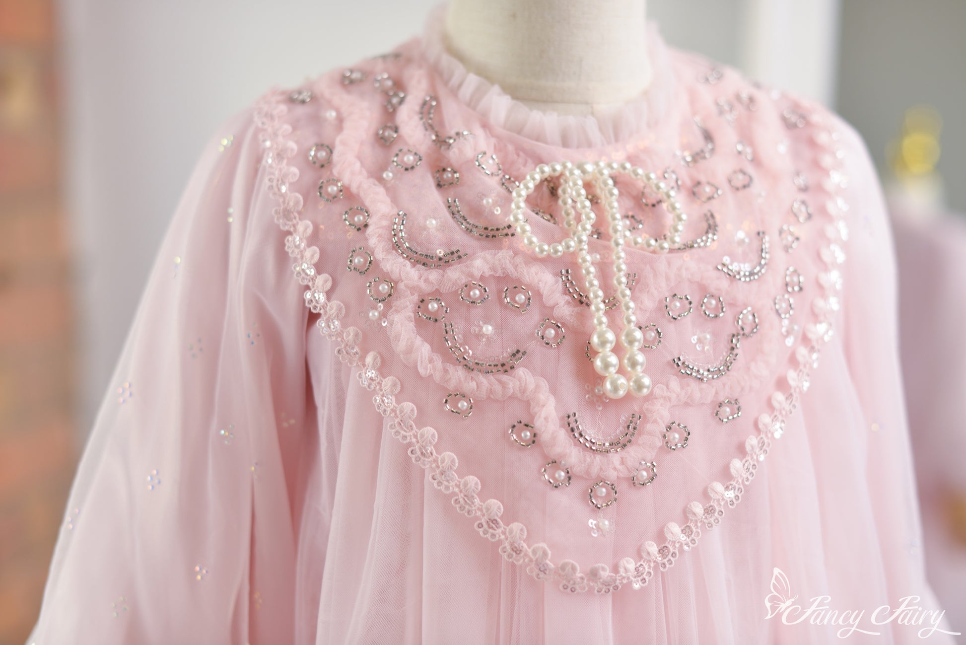 Close-up of pink lace dress front chest panel with pearl beading and bow-tie neckline.
