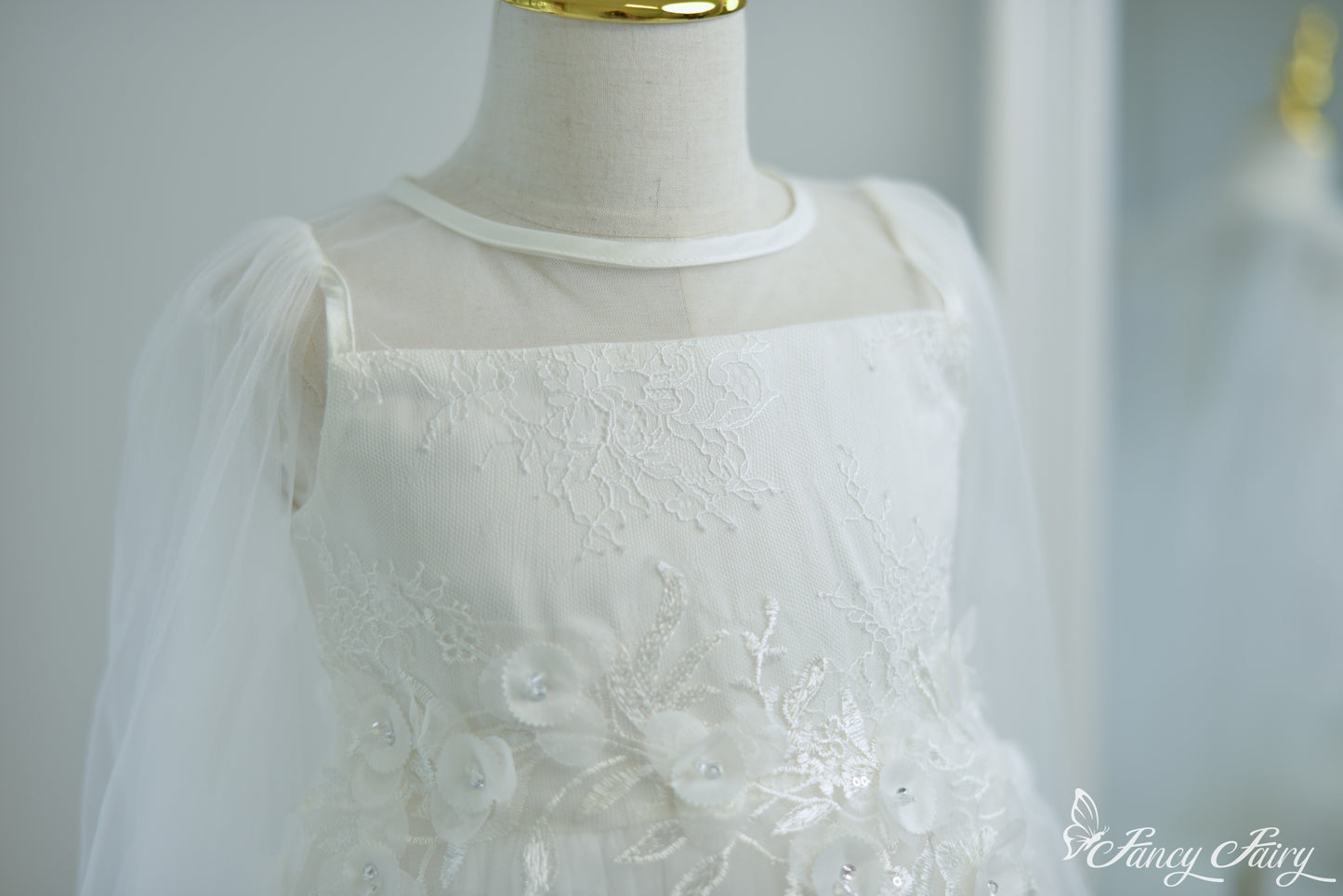 Front close-up of white girls' dress with illusion neckline, floral embroidery, and sheer tulle sleeves.